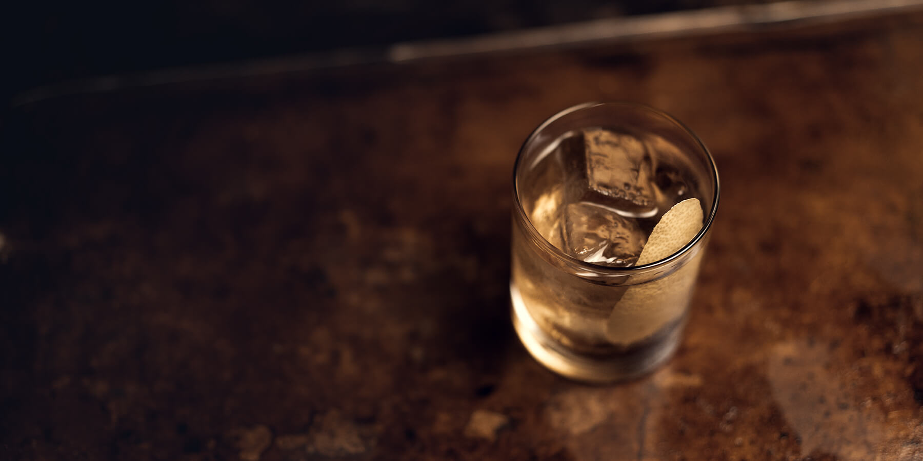 Ett tumblerglas med isbitar, lite citrusskal och drinken Rusty Nail.