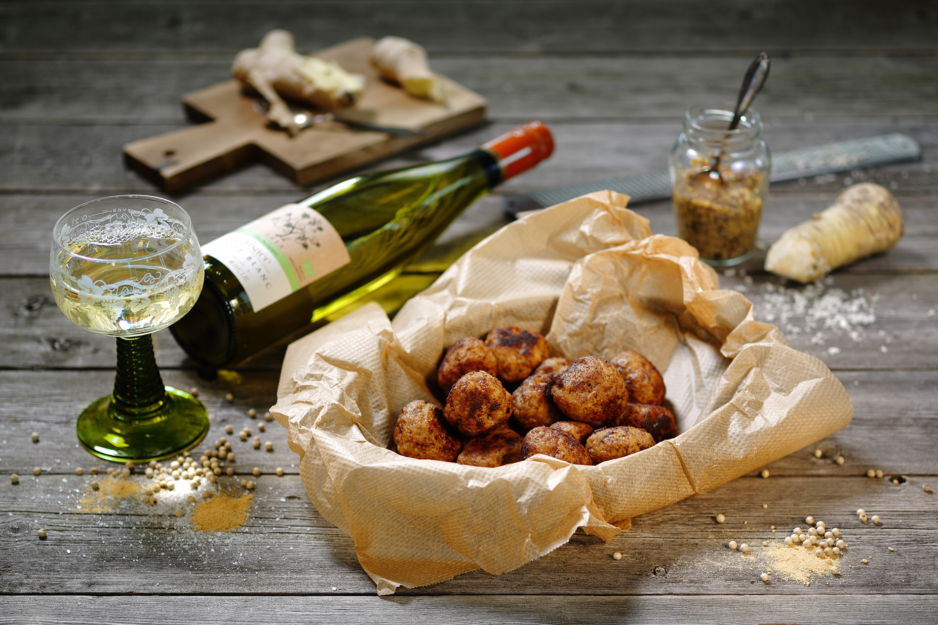 köttbullar som ligger i ett fat omgiven av papper, ett glas vitt och en liggande vinflaska bredvid
