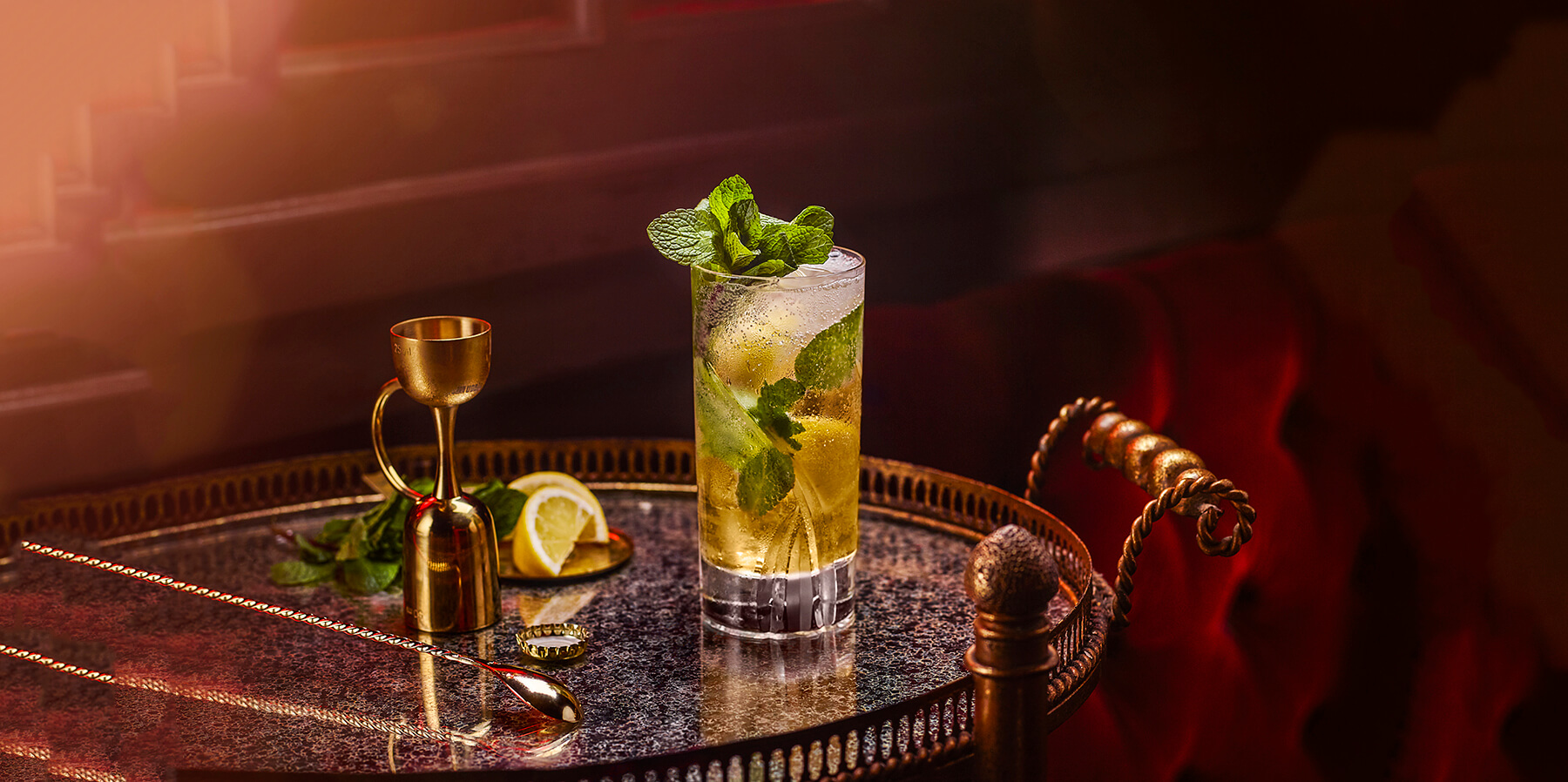 En bricka med en drinksked, centilitermått och ett glas med drinken Drambuie Collins, med is