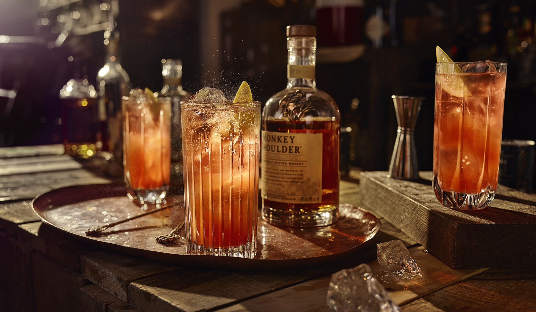 En bricka med två glas med den röd-orangea drinken Artist's Special och en flaska Monkey Shoulder.