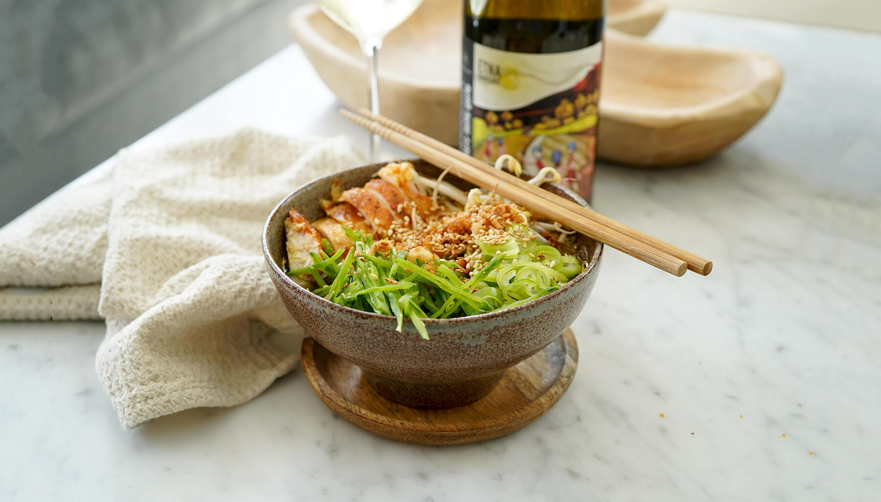 en skål ramen med kyckling och en flaska vin